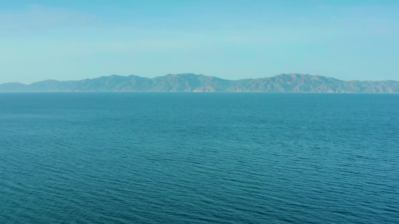 Blue sea fills most of the frame with low mountains across the horizon near El Sargento La Ventana, Mexico, and no visible people.