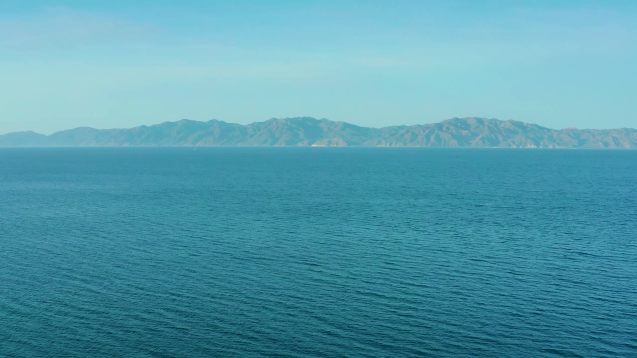 A broad field of blue water leads to a distant mountain ridge near El Sargento La Ventana, Mexico, with bright even light and no visible people.