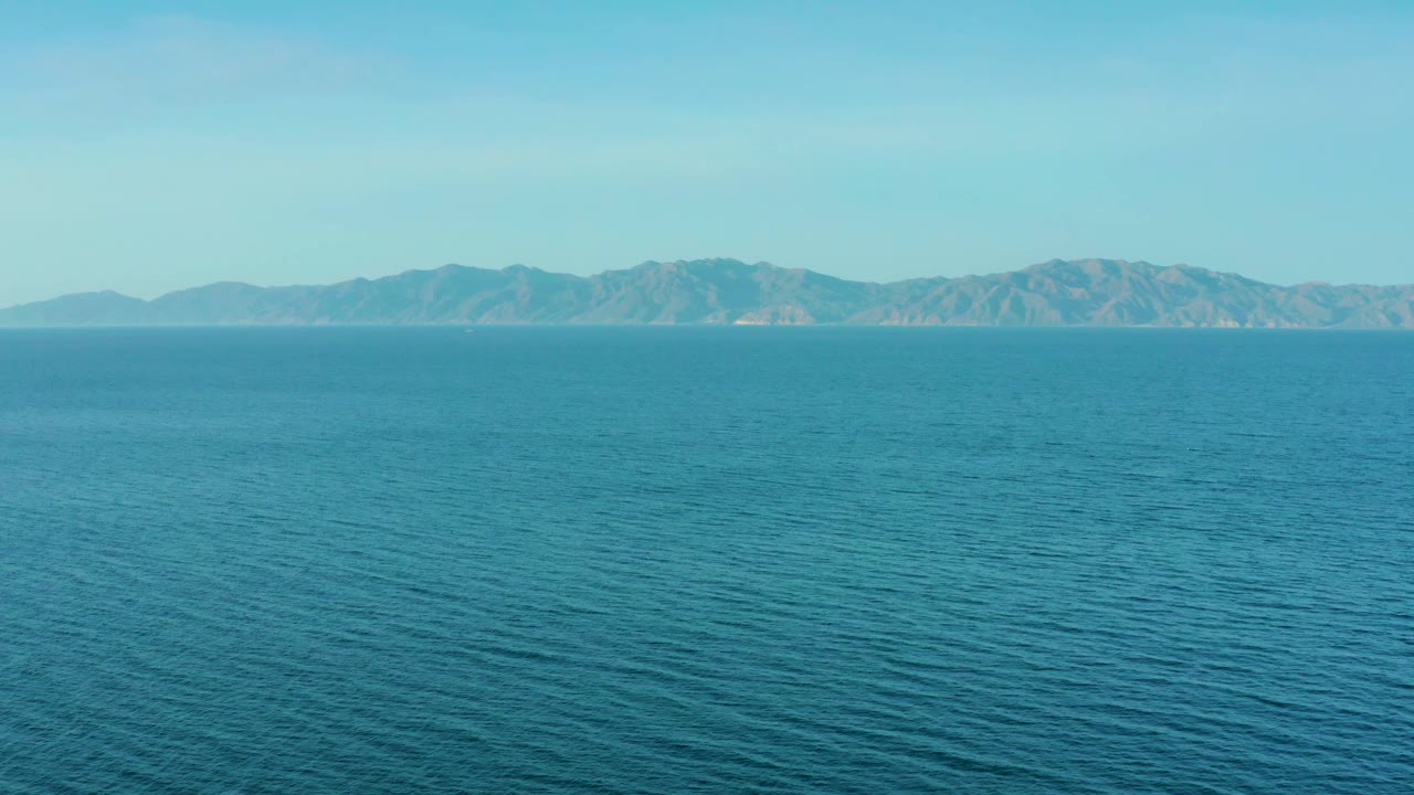At 0:02, blue sea covers most of the frame in El Sargento La Ventana, Mexico, with a continuous mountain range along the horizon and no visible people.