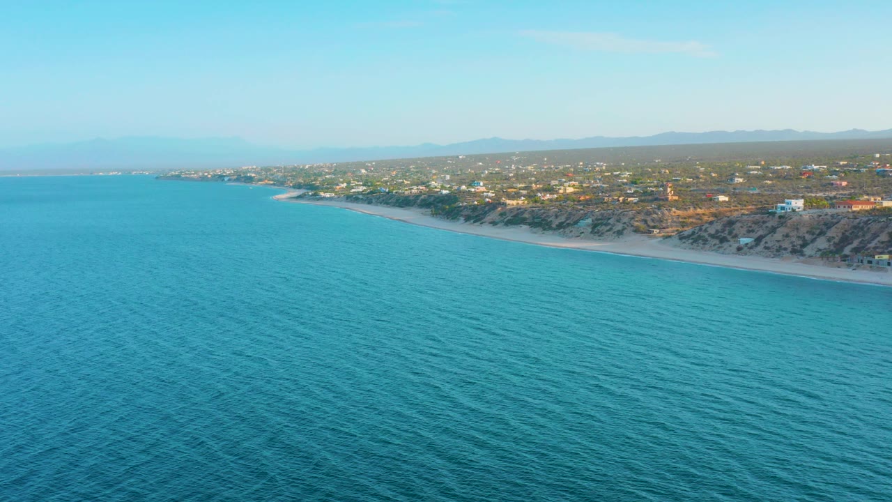 Aerial coastline view with open blue water and a beach lined by homes.