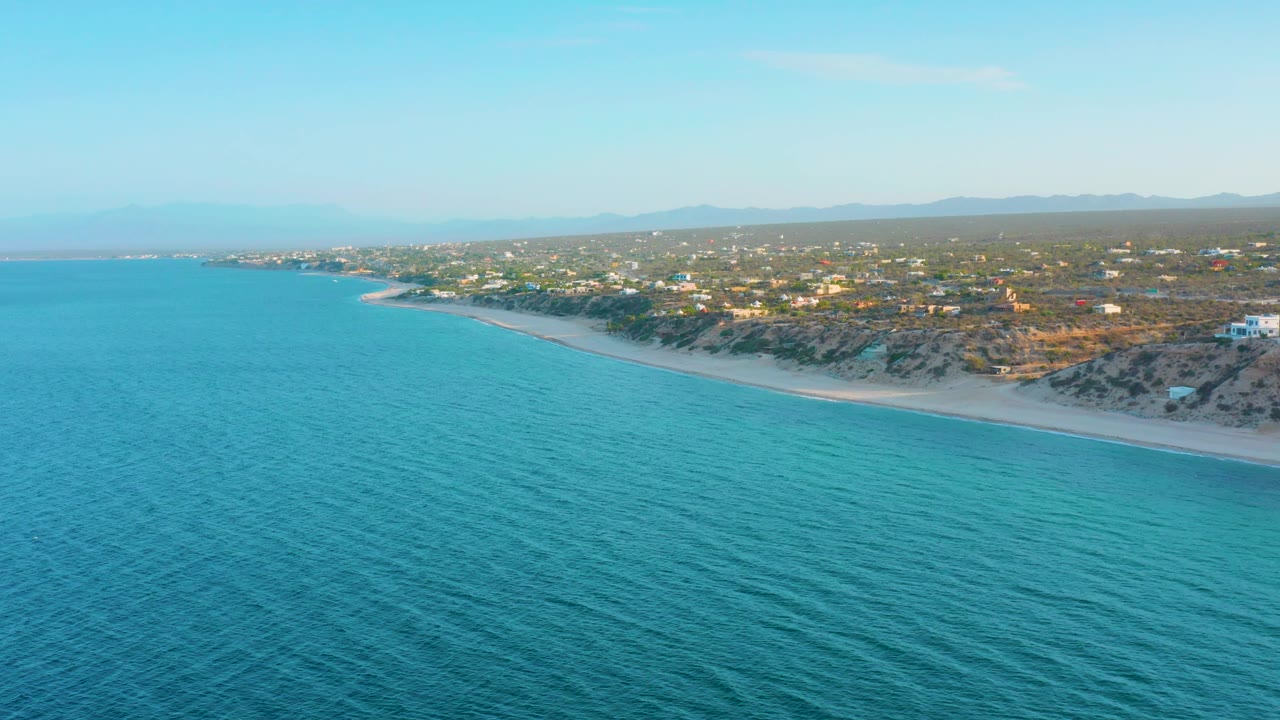 Blue ocean foreground with a long sandy shore and homes inland.