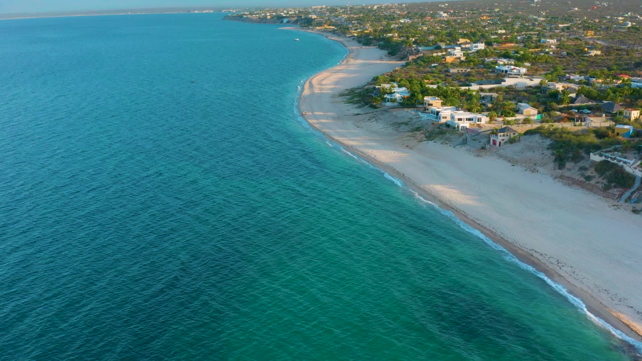 Aerial view of a sandy shoreline with turquoise water and houses above the beach.