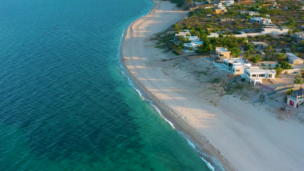 Drone-style view of a curved beach with turquoise water and beachfront houses.