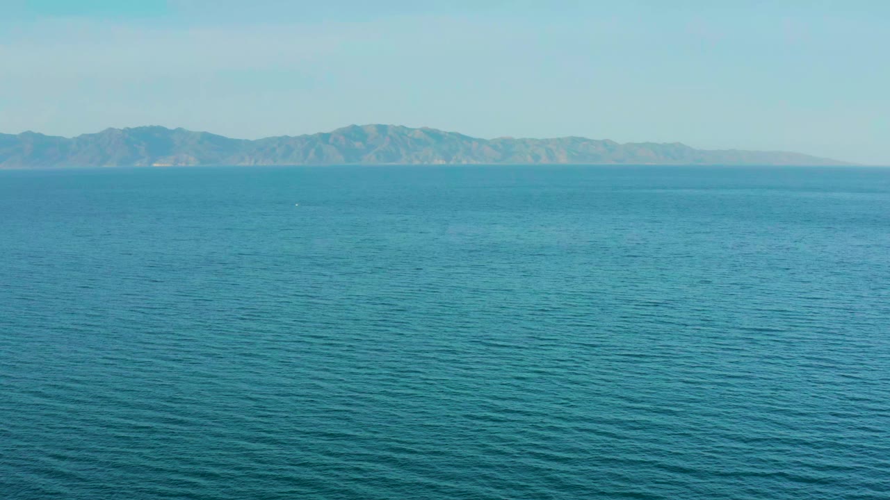 Opening frame of blue ocean off El Sargento La Ventana, Mexico, with a distant mountain coastline across the horizon and no visible people.