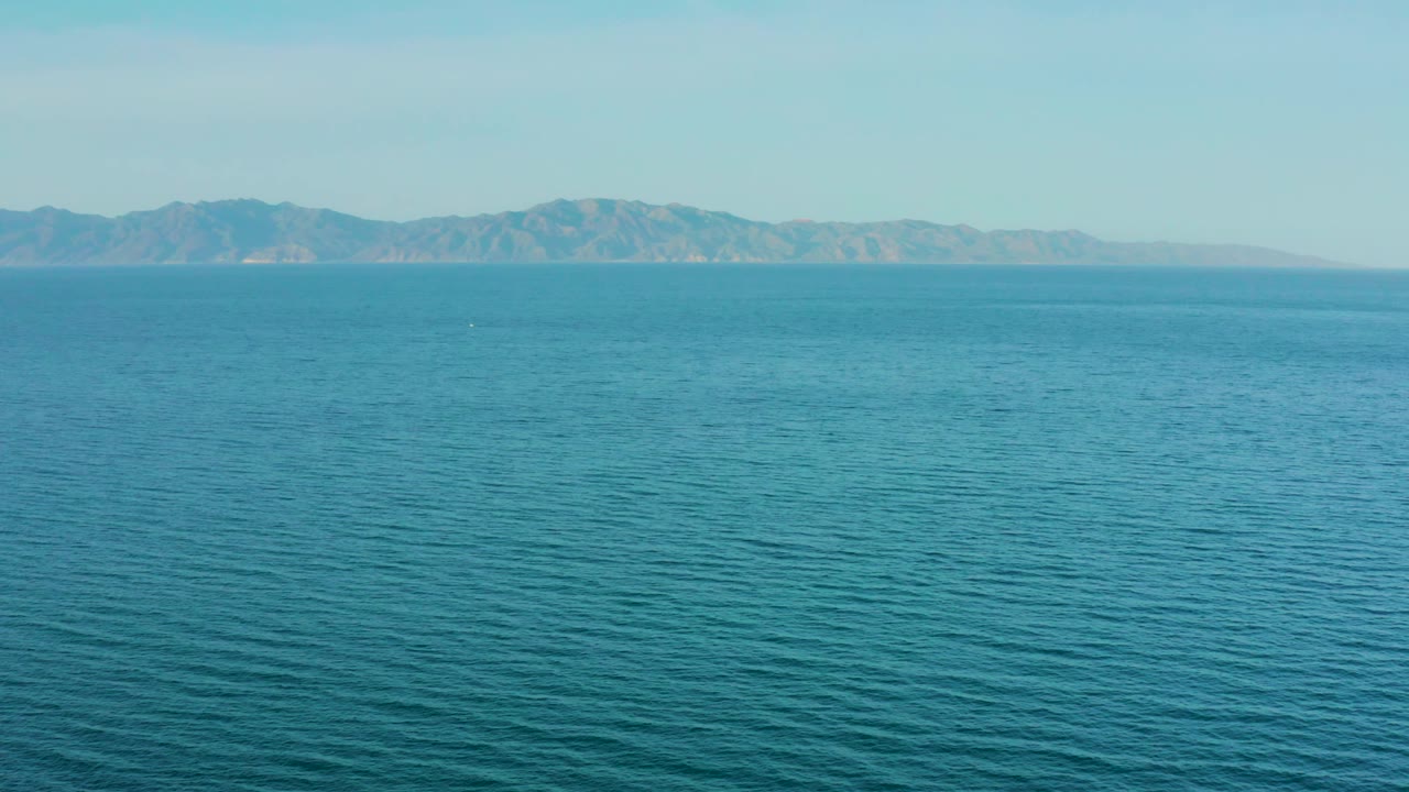 Calm blue water leads to a distant shoreline and mountain ridge near El Sargento La Ventana, Mexico, with no visible people in the frame.