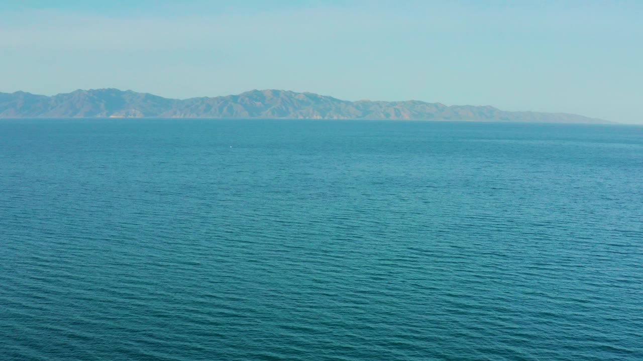 Wide view of blue ocean water and distant mountains near El Sargento La Ventana, Mexico, with no visible people.