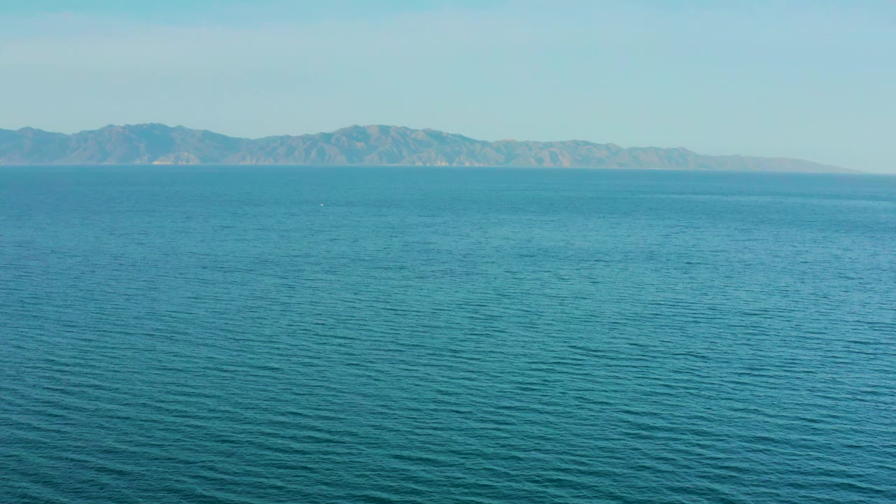Blue water fills the foreground and midground while a low mountain range sits across the horizon in El Sargento La Ventana, Mexico, with no visible people.