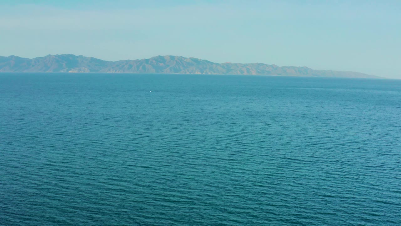 A slightly softer horizon view shows blue sea in the foreground and a distant mountain coastline near El Sargento La Ventana, Mexico, with no visible people.