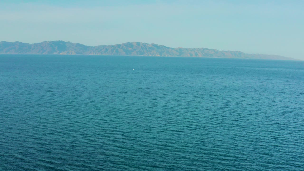 Wide elevated view of turquoise sea and distant mountains near El Sargento La Ventana, Mexico, with pale sky and no visible people.