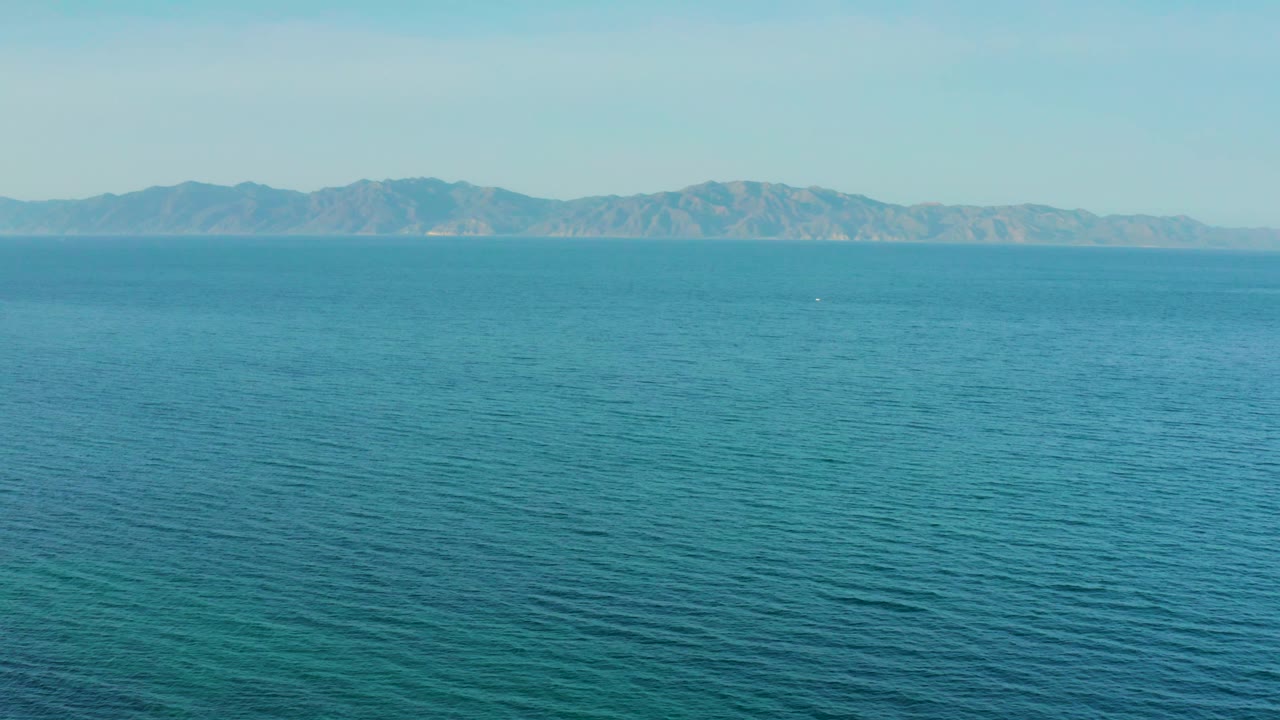 Open blue sea extends to a long mountain ridge near El Sargento La Ventana, Mexico, with faint surface texture and no visible people.