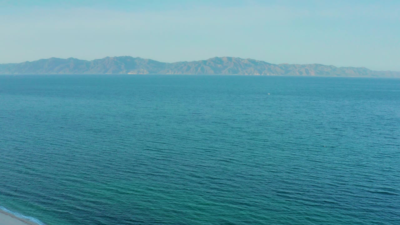 Opening frame of blue ocean off El Sargento La Ventana, Mexico, with distant mountains on the horizon, a small beach edge at lower left, and no visible people.