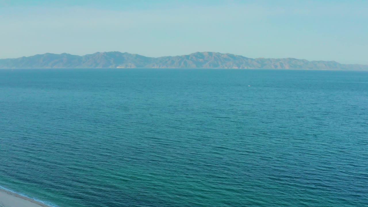 Mid-clip frame of turquoise-blue ocean near El Sargento La Ventana, Mexico, with the mountain range running across the background and no visible people.