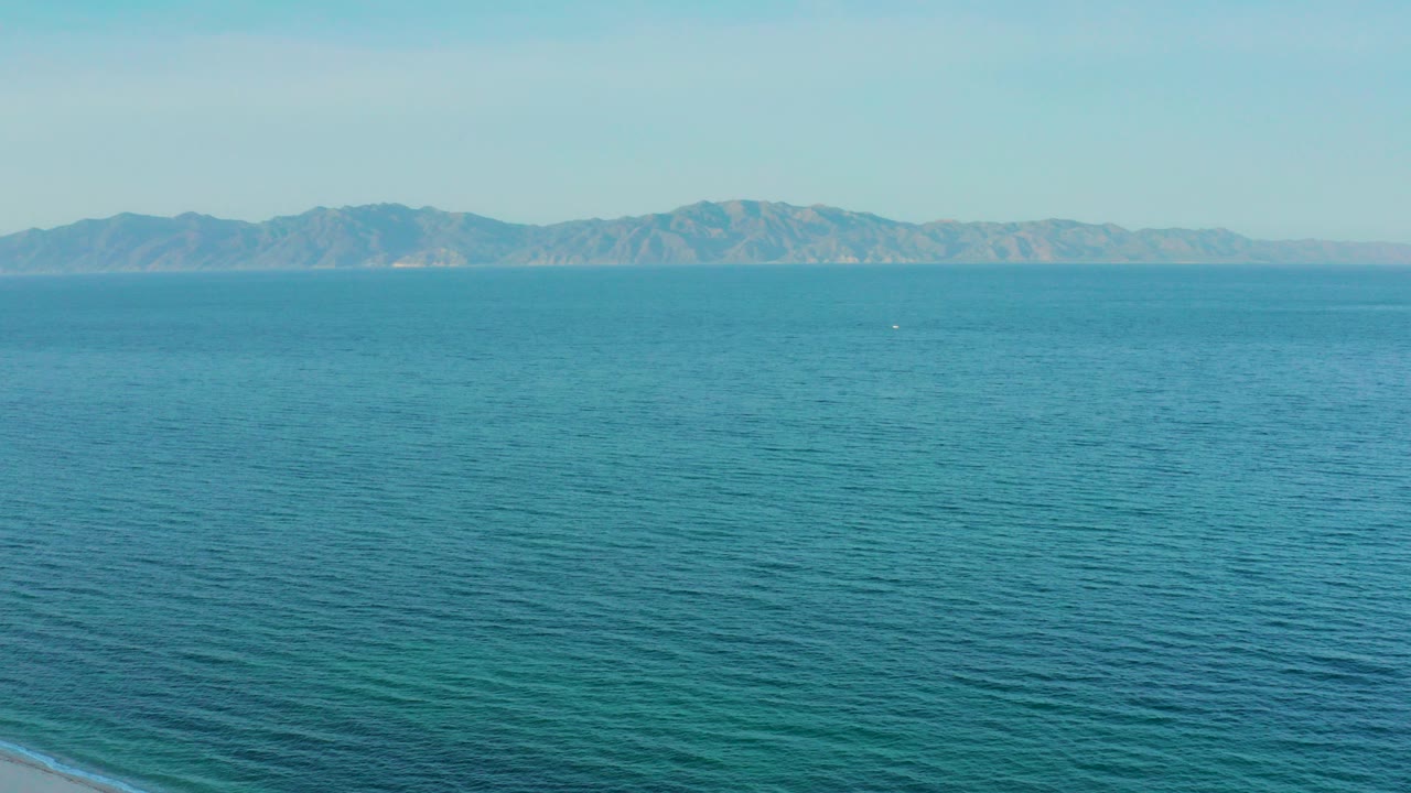 Opening frame of blue-green ocean off El Sargento La Ventana, Mexico, with distant mountains on the horizon and no visible people.