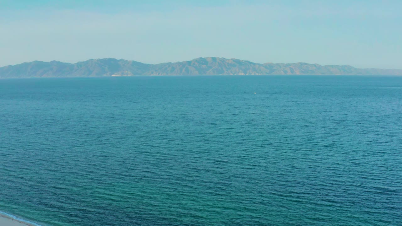 Blue ocean surface fills the foreground while the mountain range remains clear across the horizon near El Sargento La Ventana, Mexico, with no visible people.