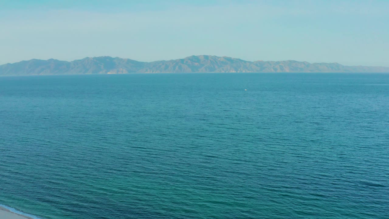 A broad field of turquoise water sits below a pale sky and distant mountains in El Sargento La Ventana, Mexico, with no visible people.