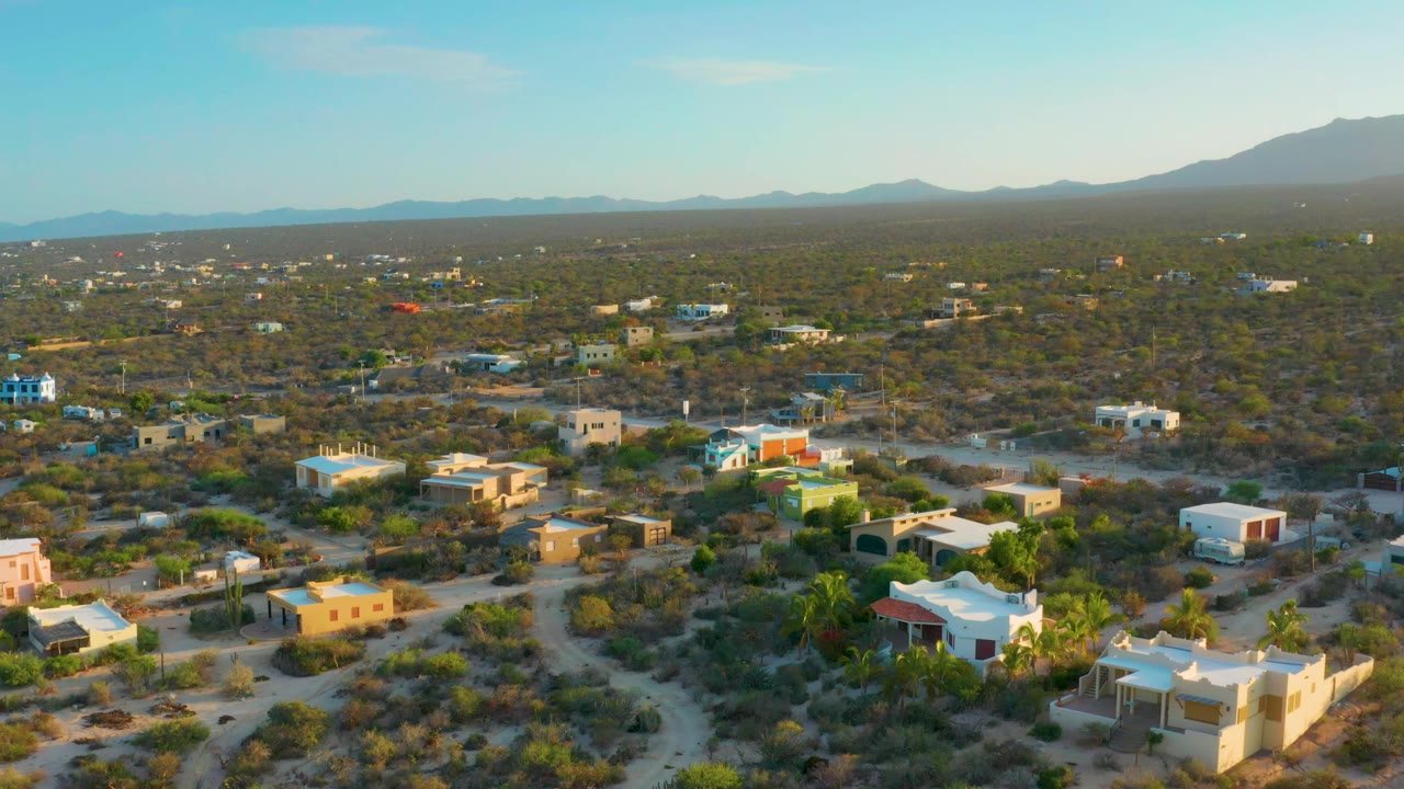 Aerial view of low houses and desert brush with mountains beyond and sea at the horizon