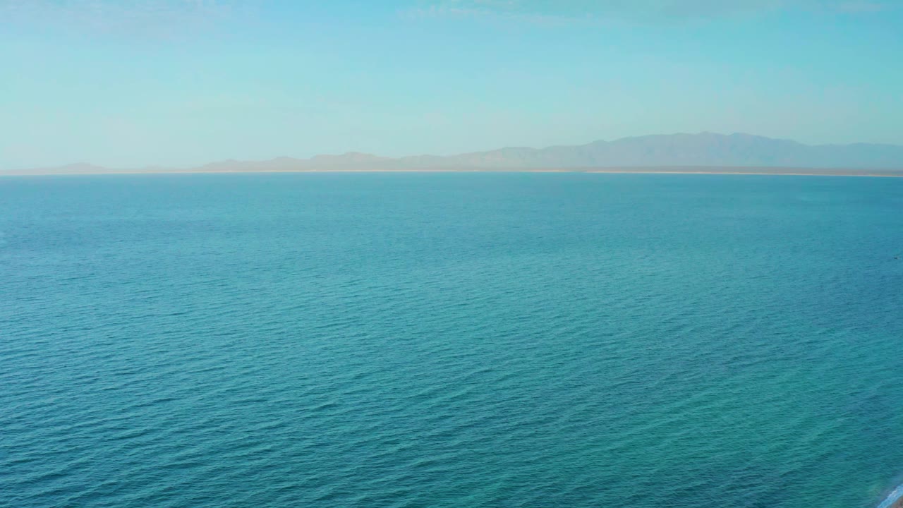 Early frame showing open blue water off El Sargento La Ventana, Mexico, with soft ripples in the foreground and a pale coastline in the distance, no visible people.