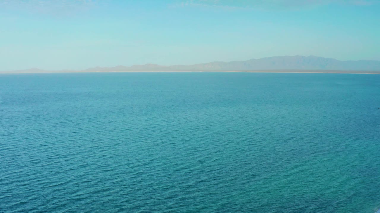Mid-early view of teal and blue ocean near El Sargento La Ventana, Mexico, with the distant mountain ridge slightly clearer along the upper edge, no visible people.