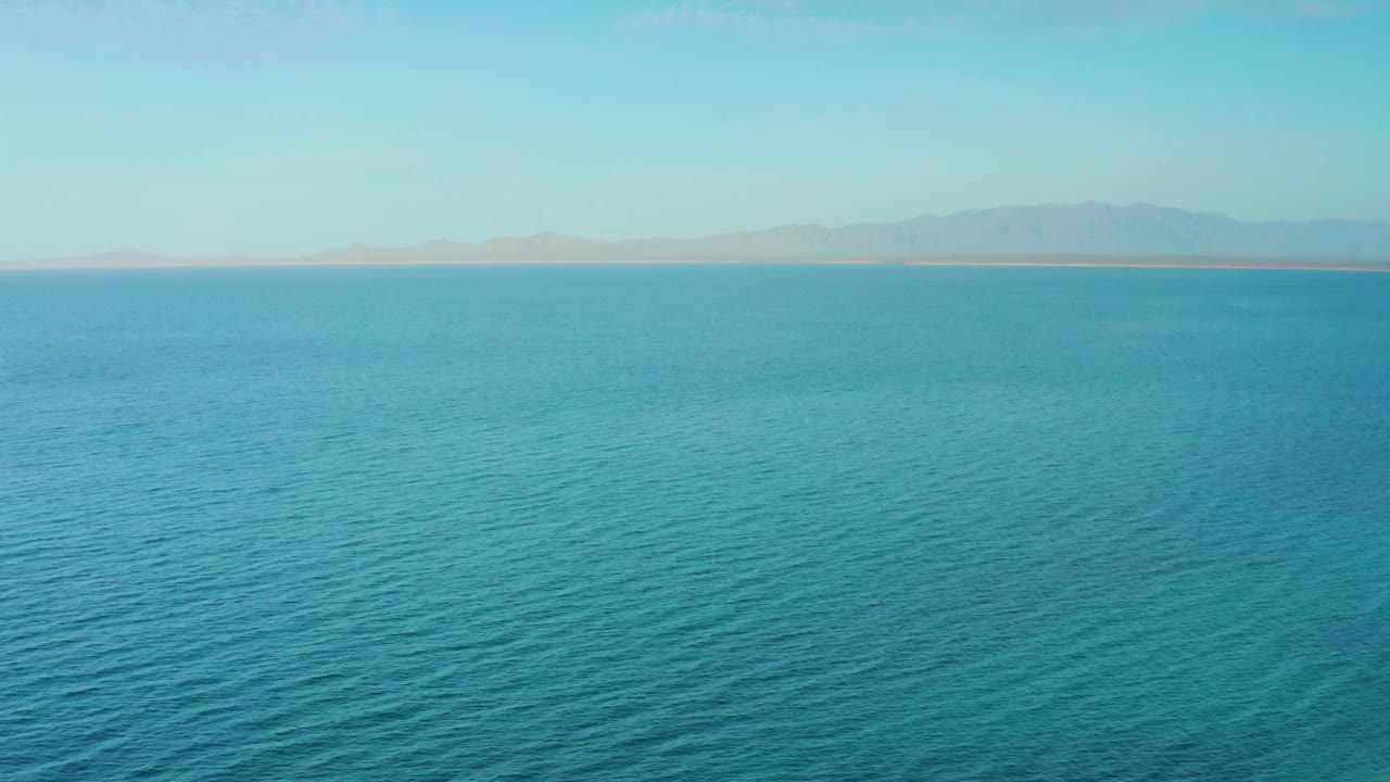 Central runtime frame of expansive ocean off El Sargento La Ventana, Mexico, with bright daylight across the water and a low shoreline behind it, no visible people.
