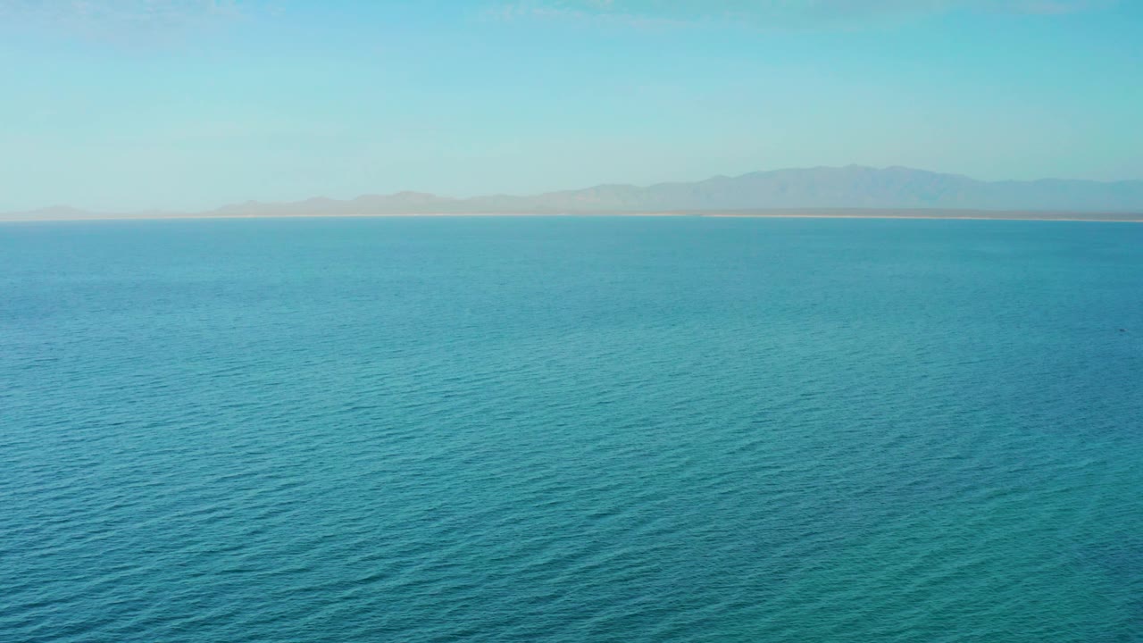 Open turquoise water stretches toward a thin shoreline and distant mountains near El Sargento La Ventana, Mexico, with no visible people or vessels.