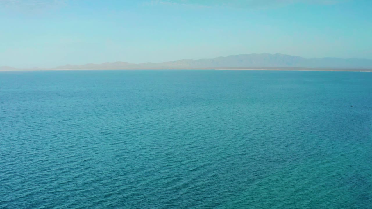 Elevated view of turquoise water with low ripples and distant mountains along the horizon near El Sargento La Ventana, Mexico, with no visible people.
