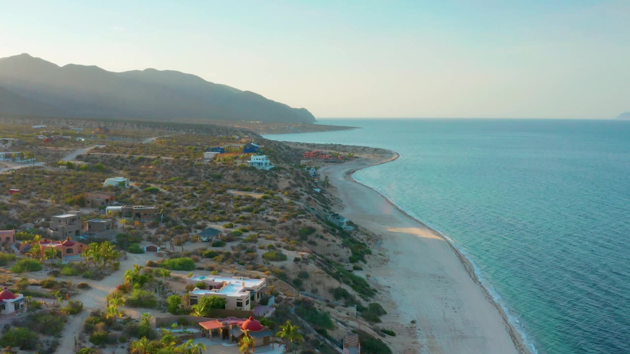 Aerial coastline with homes, scrubland, beach, and blue water
