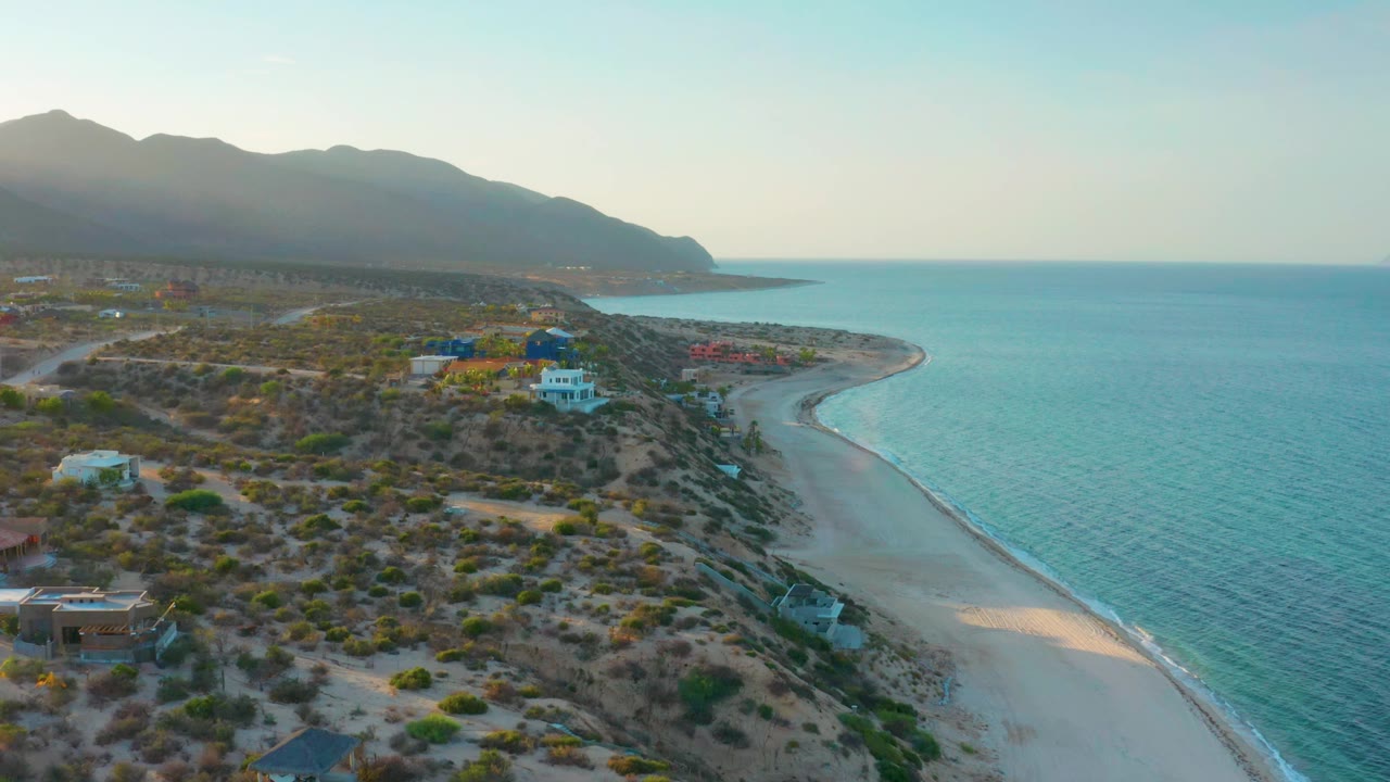 Drone view of a dune neighborhood beside a curving shoreline.