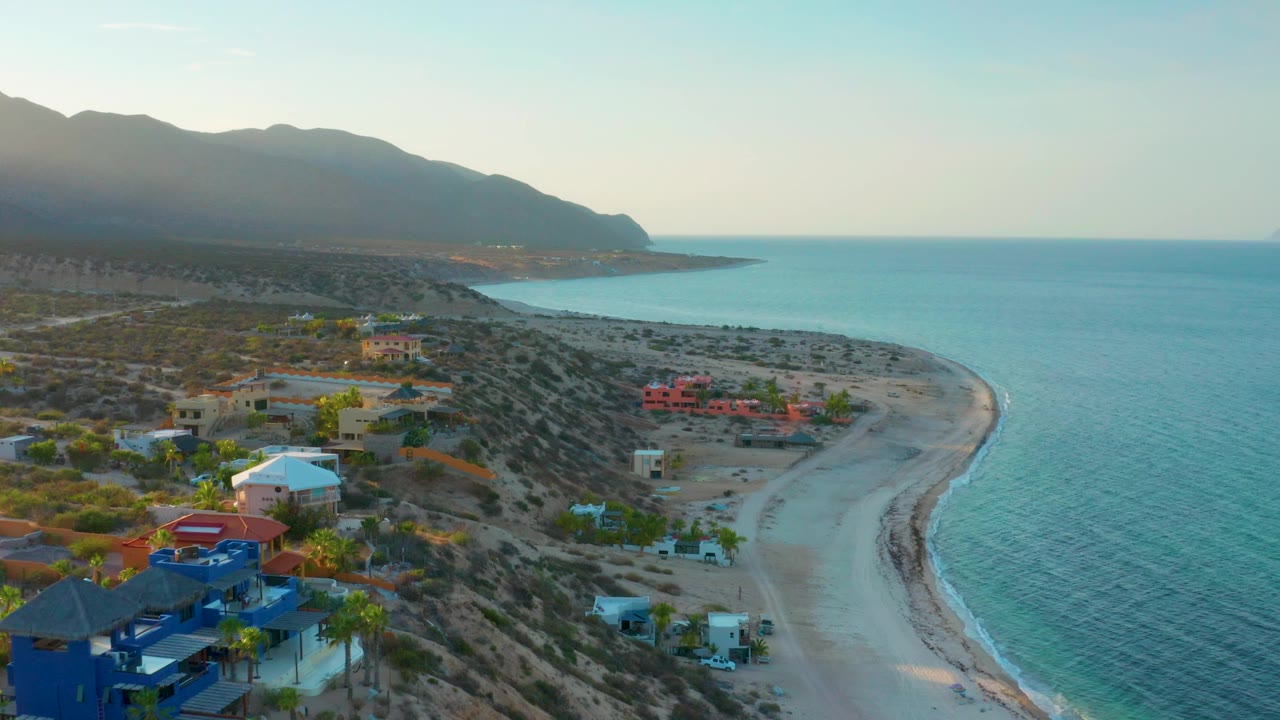 Aerial coastline with houses at lower left and blue water to the right.