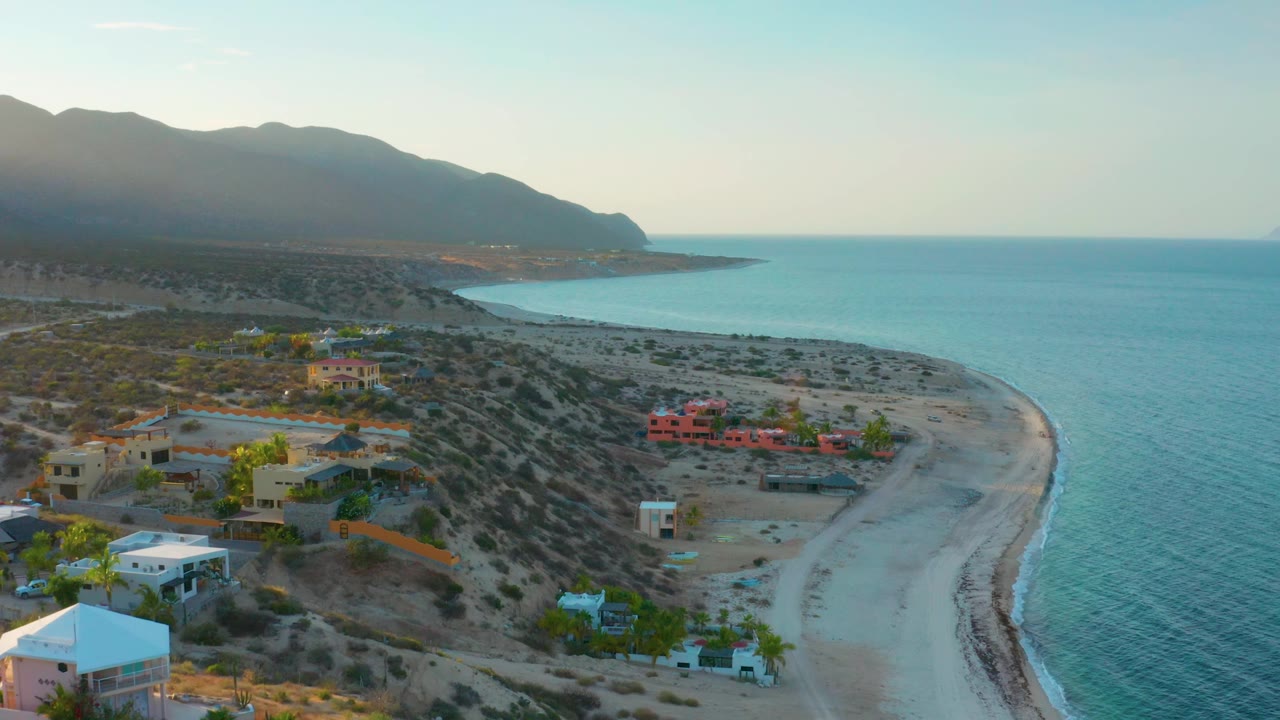 Elevated view of beach homes, desert scrub, curving sand, and calm blue water.