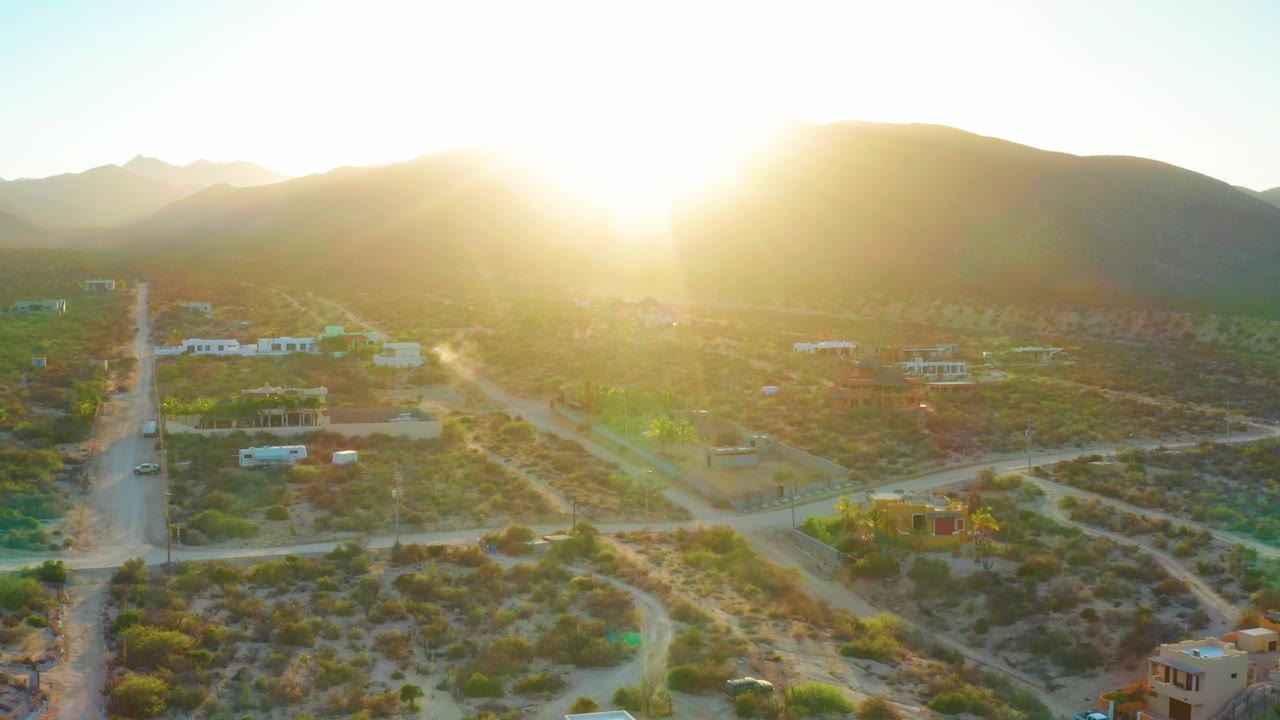 Bright sun over a hill with rural dirt roads and low buildings below.