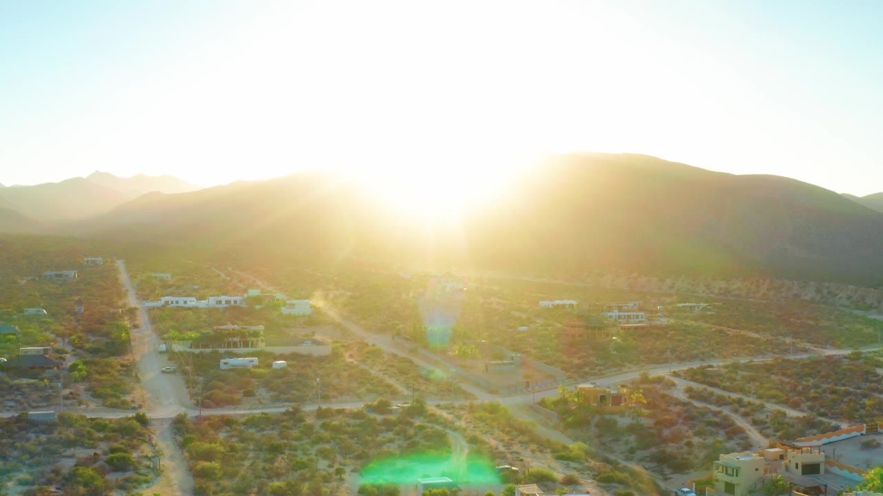 Bright sunrise over desert roads, houses, and low hills.