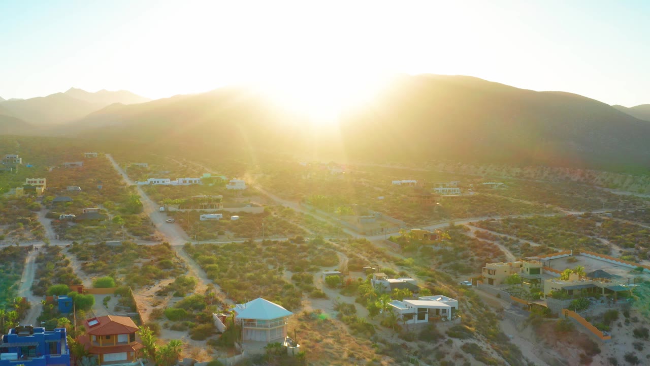Aerial view of houses below sunlit mountains