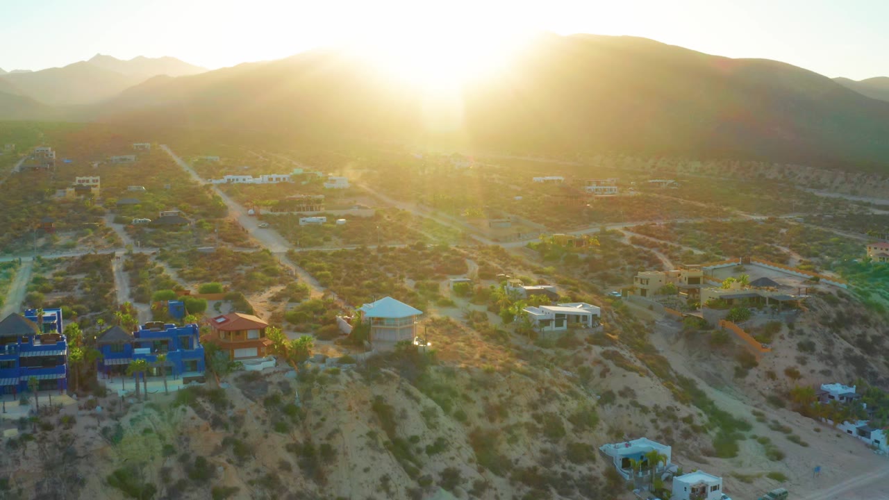 Bright sunrise above roads, desert lots, homes, and distant mountains.