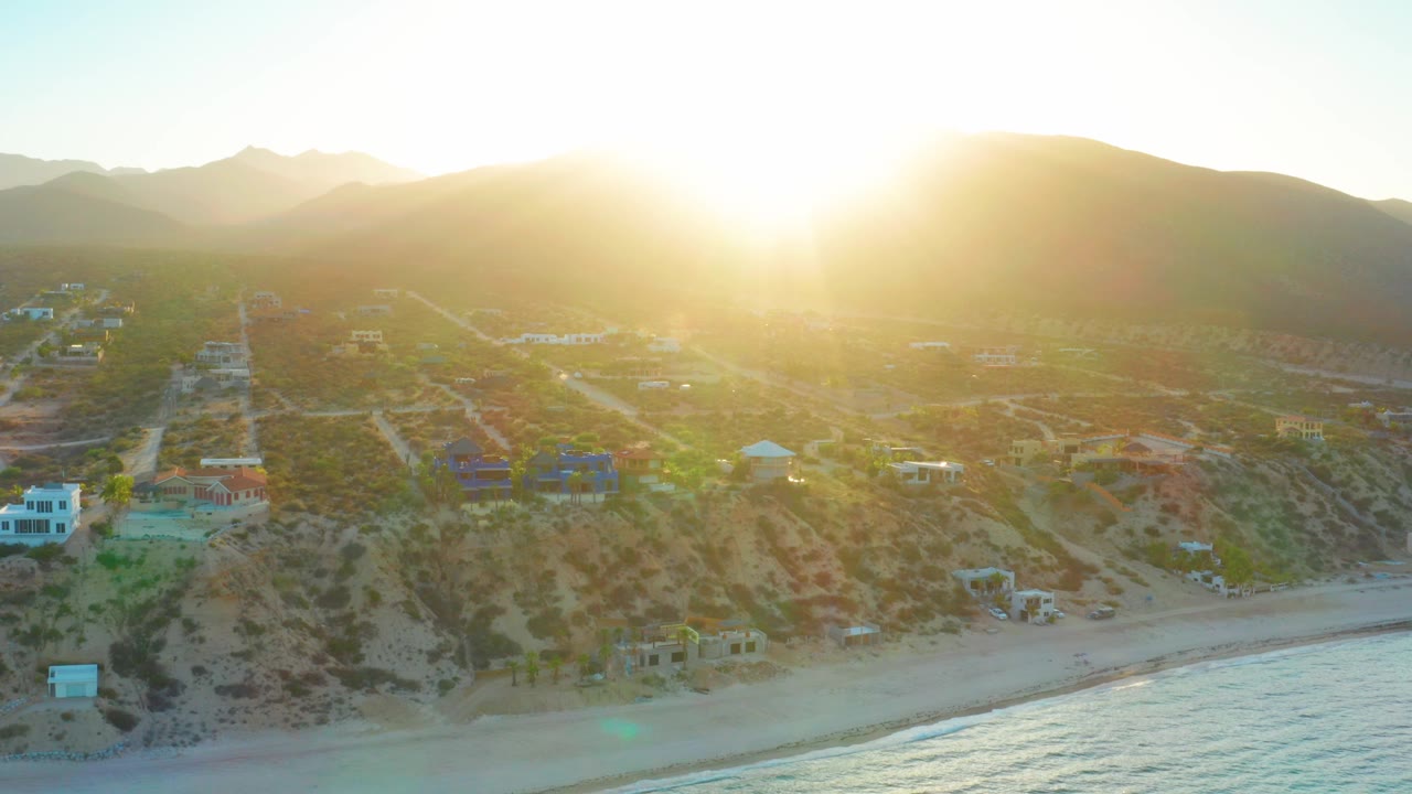 Coastal homes and dirt roads under sunrise glare beside the sea