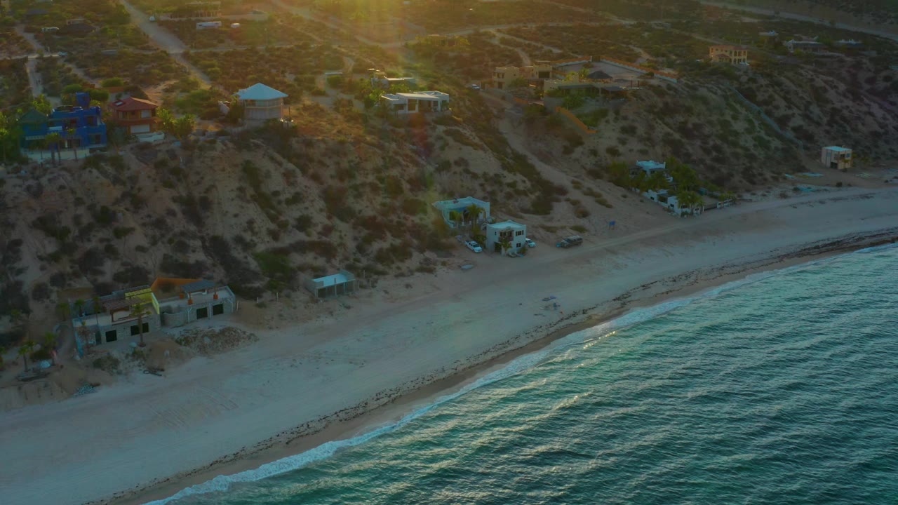 Aerial coastline with empty sand, bright surf edge, and hillside houses