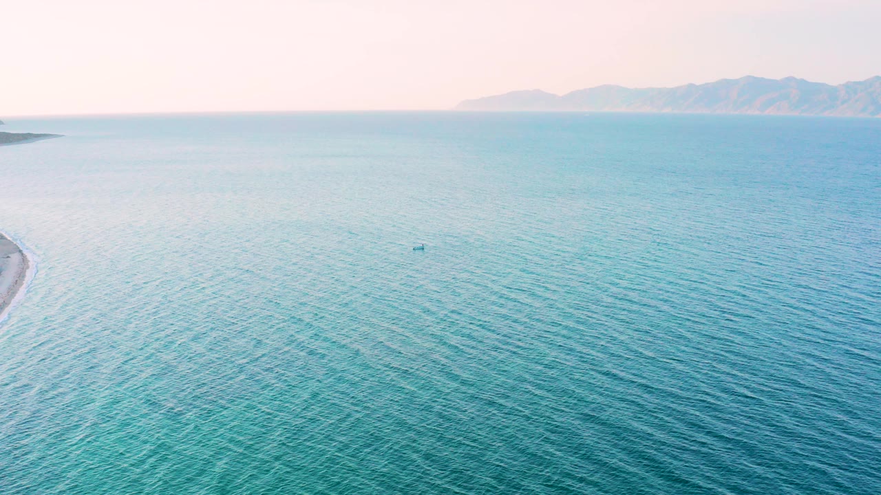 Opening frame of blue-green sea off El Sargento La Ventana, Mexico, with distant mountainous shore under a pale sky and no visible people.