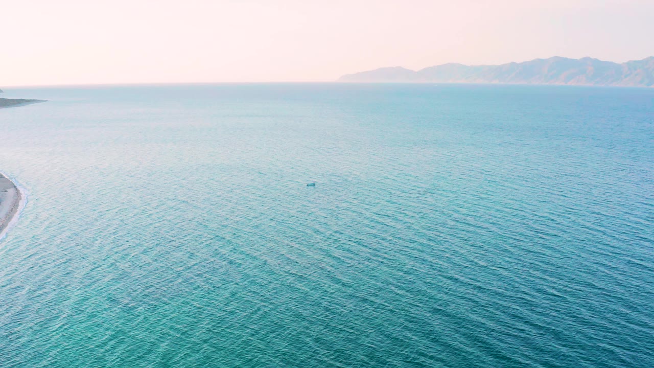 Aerial-looking frame over rippled blue water near El Sargento La Ventana, Mexico, with a sliver of shoreline at left and no visible people.