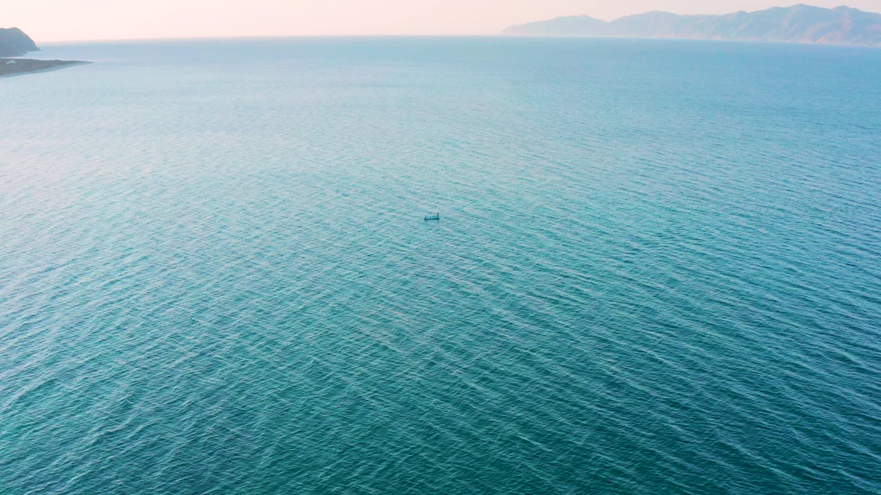 Aerial sea view with pale mountains and a small object on the water.