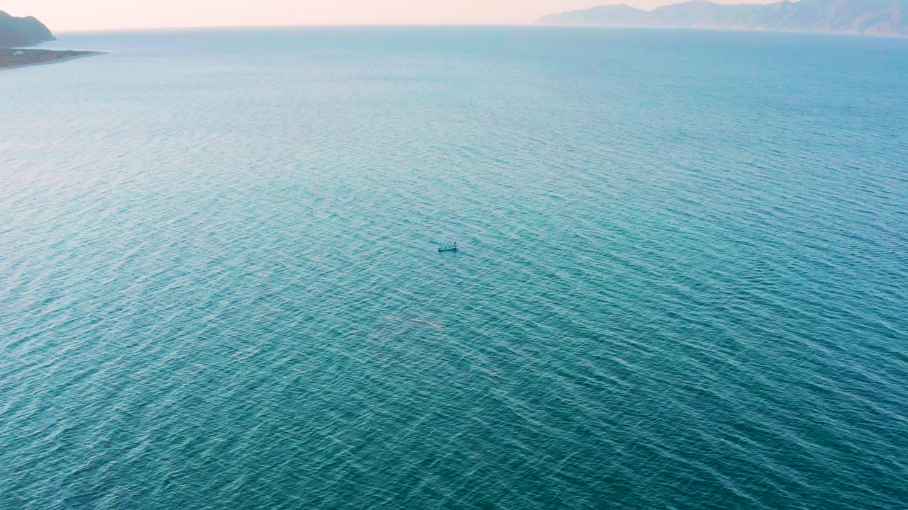 Aerial view in El Sargento La Ventana, Mexico, with the kayak slightly right of center, textured turquoise water below it, hazy distant land, and no visible people.
