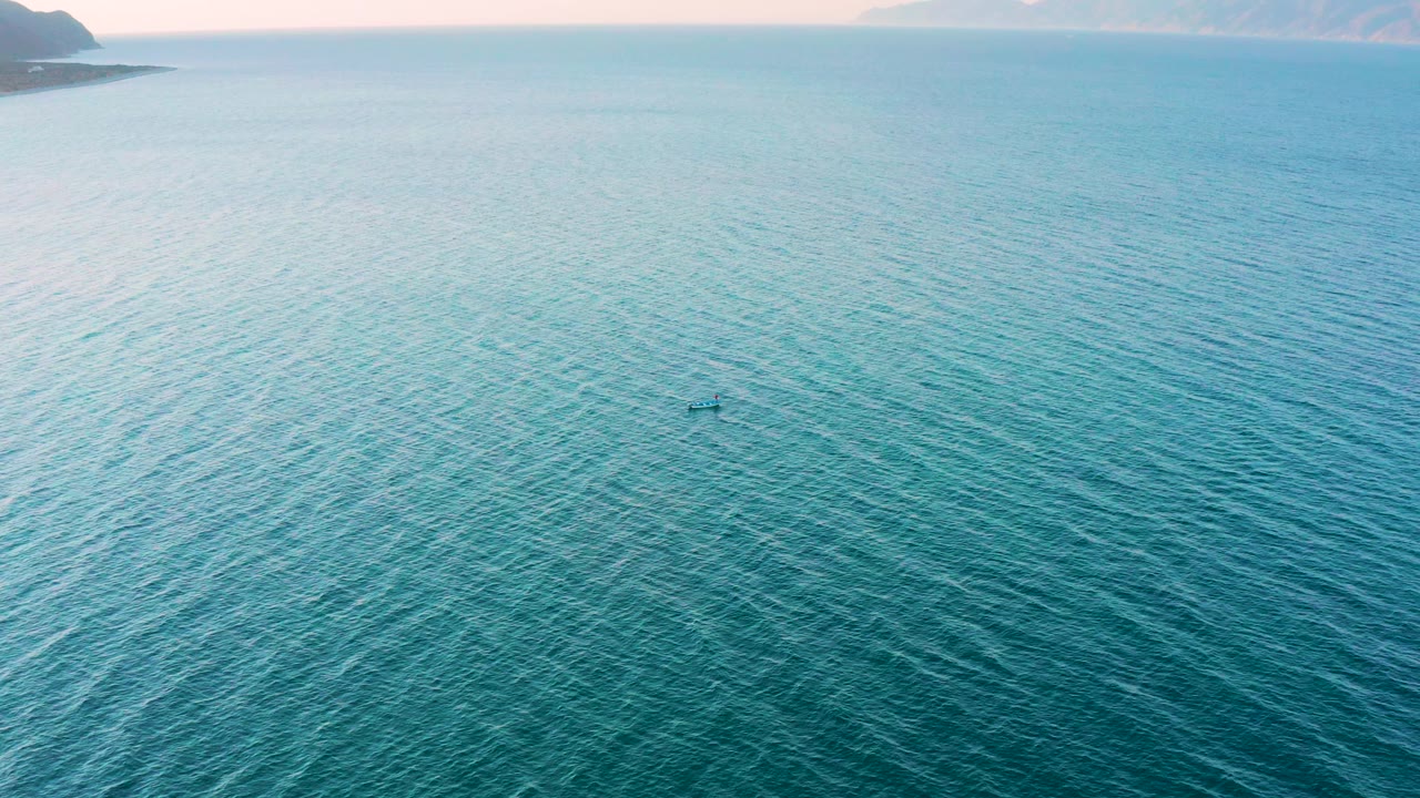 Aerial view of turquoise sea in El Sargento La Ventana, Mexico, with the kayak lower in the frame, pale water texture around it, distant coastal land at the top left, and no visible people.