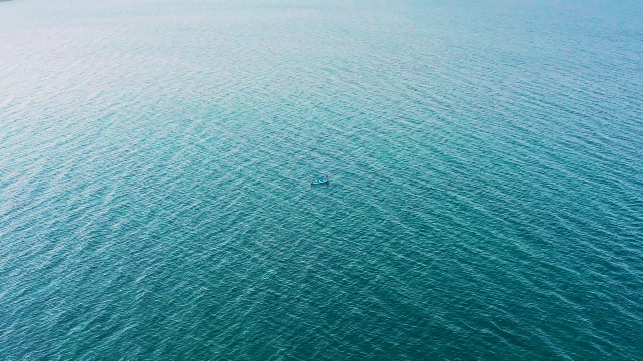 High aerial view over blue-green water in El Sargento La Ventana, Mexico, with fine surface ripples and a small boat-like object near center, no visible people.