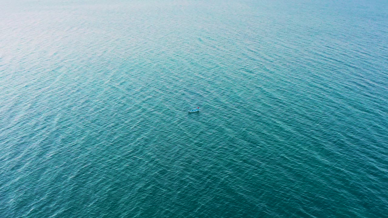 Drone view over open blue ocean in El Sargento La Ventana, Mexico, with pale reflected light at the upper left and a small boat-like object near the center, no visible people.