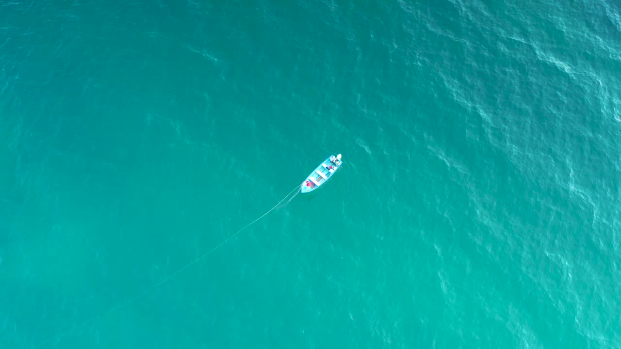 Top-down aerial frame of a small white boat on turquoise water in El Sargento La Ventana, Mexico, with faint ripples and no visible people.