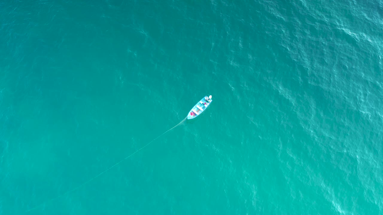 The boat appears near the top edge of the frame over turquoise sea, with a curved faint trail behind it and no shoreline or visible people.