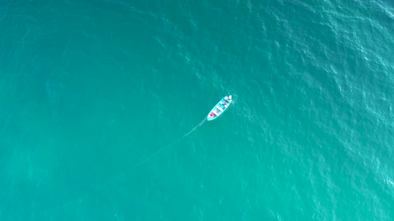 Overhead view of the small sailboat slightly farther across open turquoise water in El Sargento La Ventana, Mexico, with ripples and no visible people.