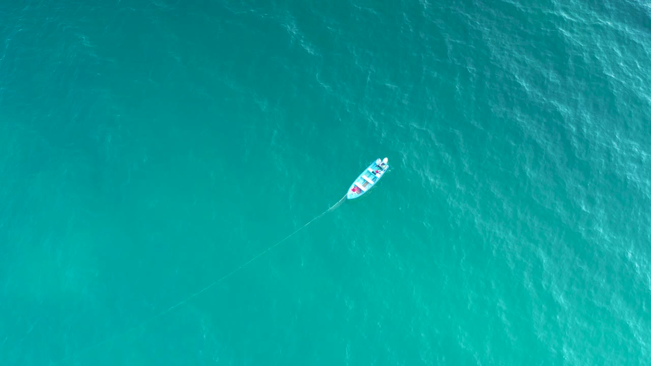 High aerial frame showing the sailboat near the upper right over textured turquoise ocean in El Sargento La Ventana, Mexico, with no shoreline and no visible people.