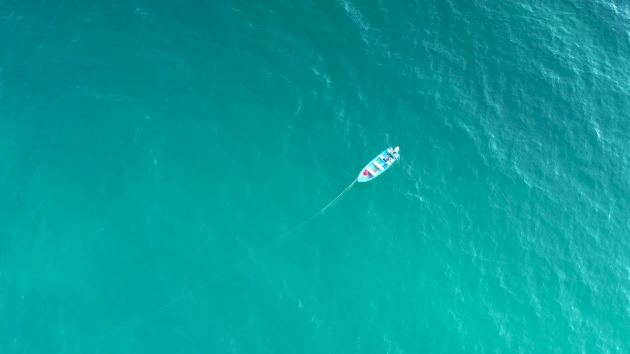 Small white boat on turquoise water from above.