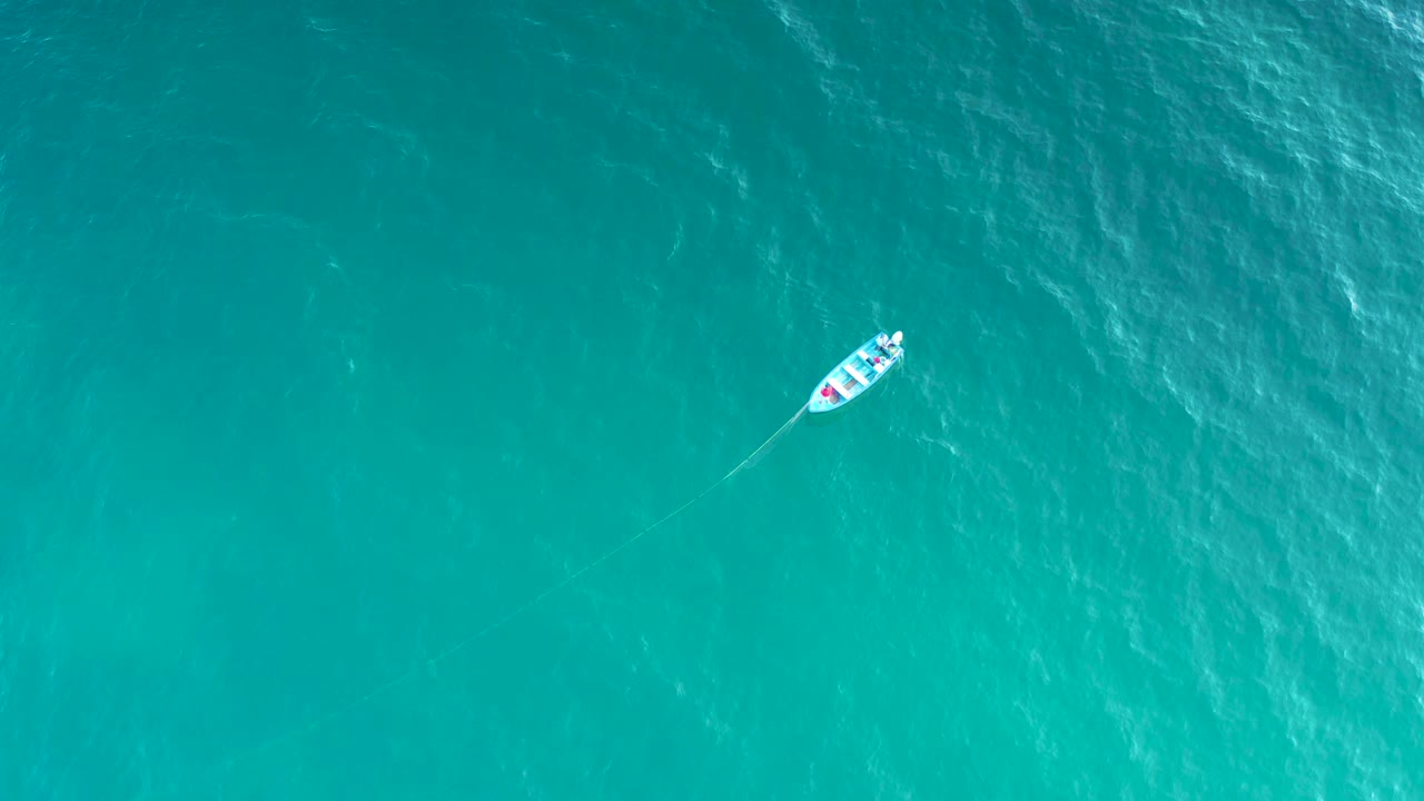 A small white boat sits slightly left of center in clear blue-green water near El Sargento La Ventana, Mexico, with a thin wake trailing behind and no visible people.