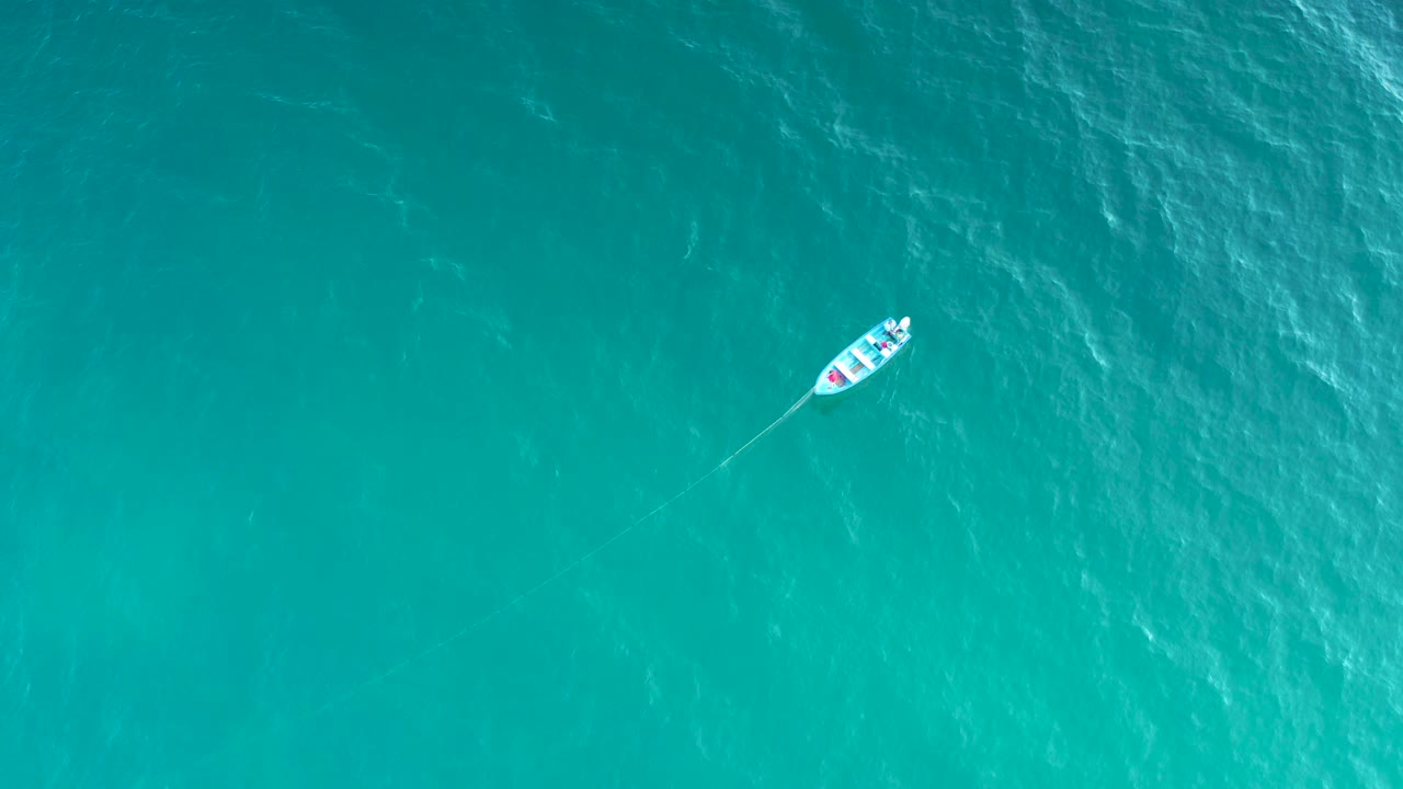The white boat appears in the upper portion of a top-down turquoise ocean frame near El Sargento La Ventana, Mexico, with pale wake marks and no visible people.