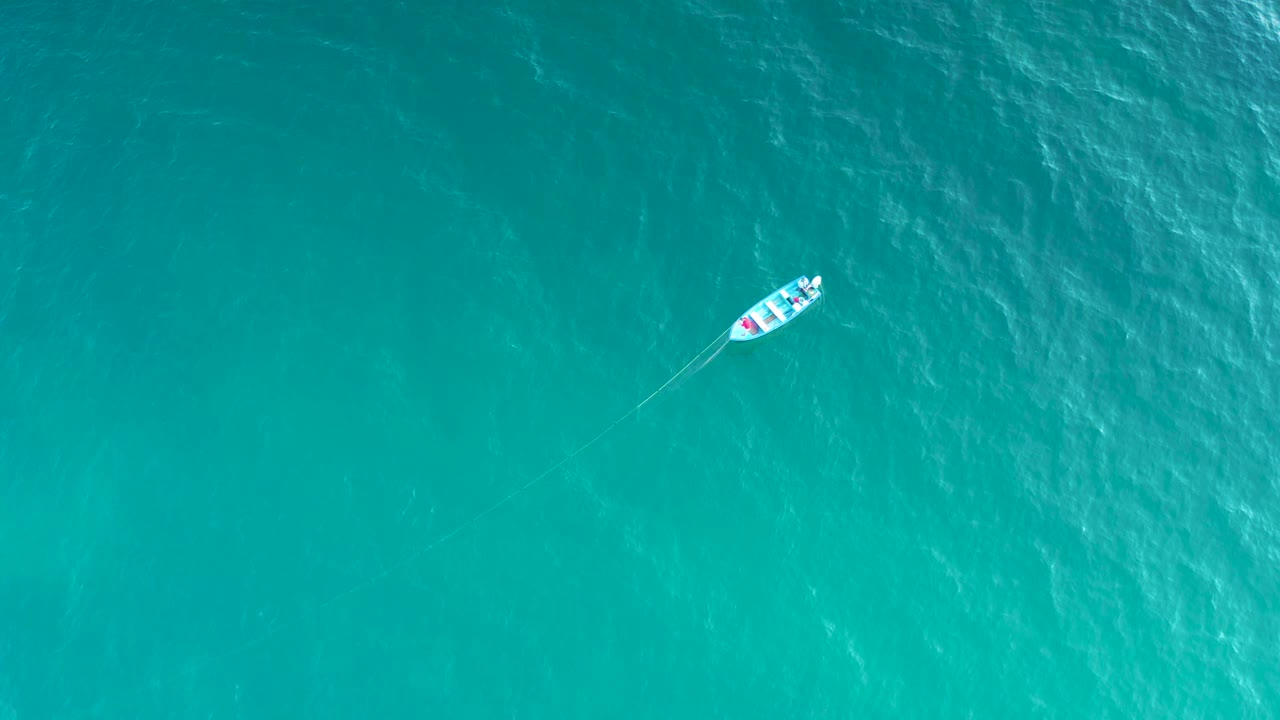 A small white boat sits near the top of a wide aerial frame over rippled blue-green water in El Sargento La Ventana, Mexico, with no visible people.